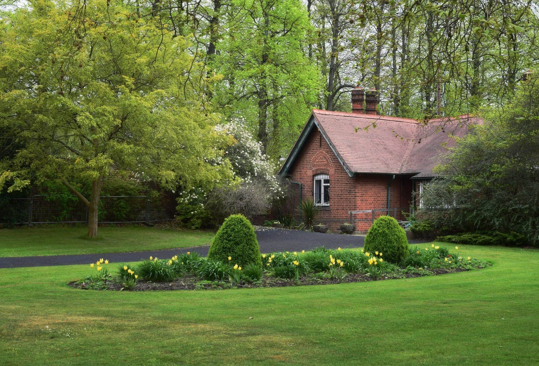 A brick bungalow with a red tiled roof set back behind a lawn and flower bed