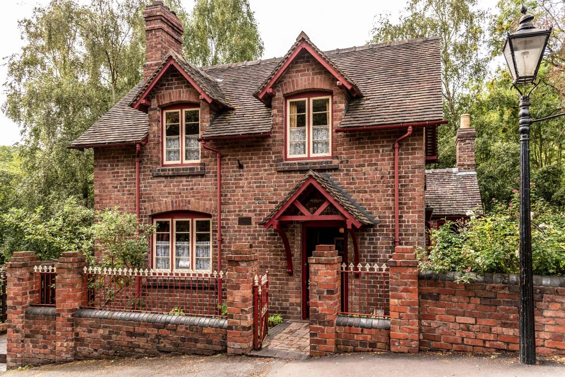 A red-brick detached cottage with painted gutters and downpipes behind a brick wall