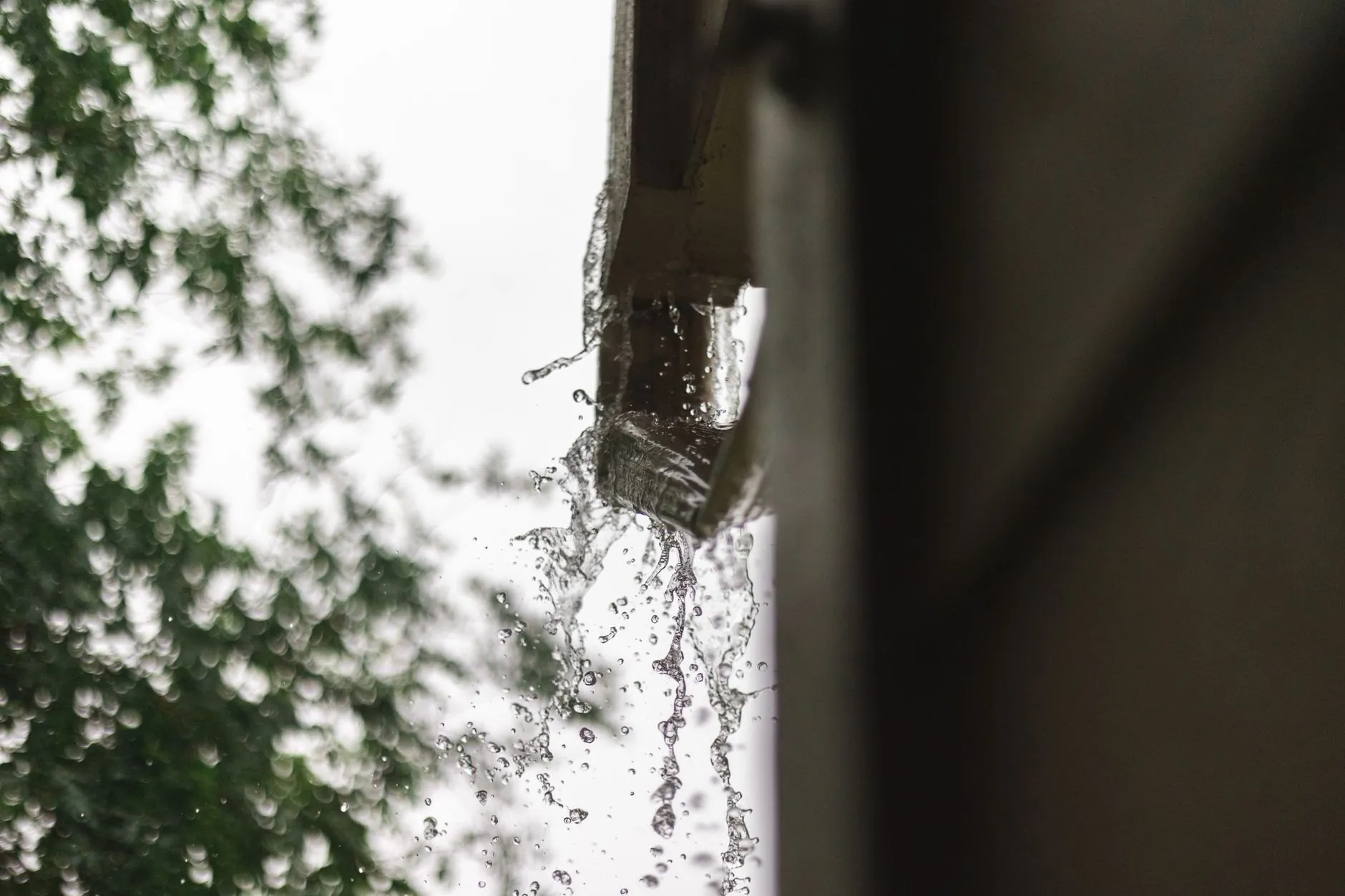 Rainwater bursting out of the top of a blocked downpipe outlet during a heavy shower